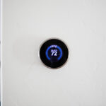 Smart thermostat mounted on a white wall displaying 72°F cooling temperature in a modern home office.