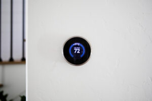 Smart thermostat mounted on a white wall displaying 72°F cooling temperature in a modern home office.
