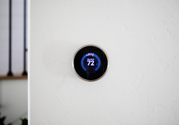 Smart thermostat mounted on a white wall displaying 72°F cooling temperature in a modern home office.