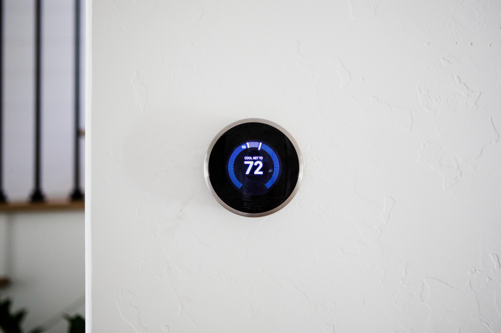 Smart thermostat mounted on a white wall displaying 72°F cooling temperature in a modern home office.