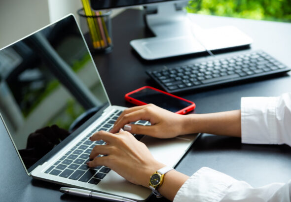 programmer typing code on laptop at modern workspace with smartphone and keyboard