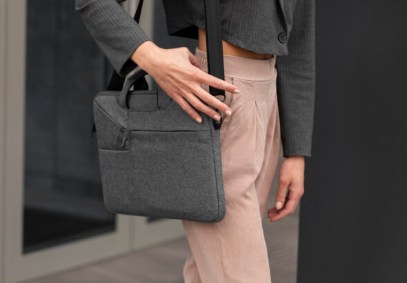 Professional carrying a gray laptop sleeve bag with shoulder strap, paired with business attire in a modern office setting.