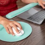 Hand using an ergonomic mouse pad with wrist support next to a laptop, ideal for programming and gaming setups