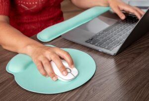 Hand using an ergonomic mouse pad with wrist support next to a laptop, ideal for programming and gaming setups