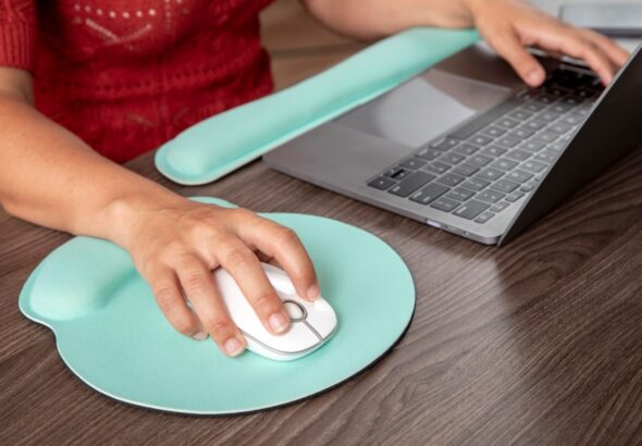 Hand using an ergonomic mouse pad with wrist support next to a laptop, ideal for programming and gaming setups
