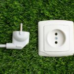 White European-style power plug and matching wall socket module placed on green artificial grass, symbolizing smart plug technology and energy-conscious home offices.