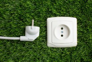 White European-style power plug and matching wall socket module placed on green artificial grass, symbolizing smart plug technology and energy-conscious home offices.