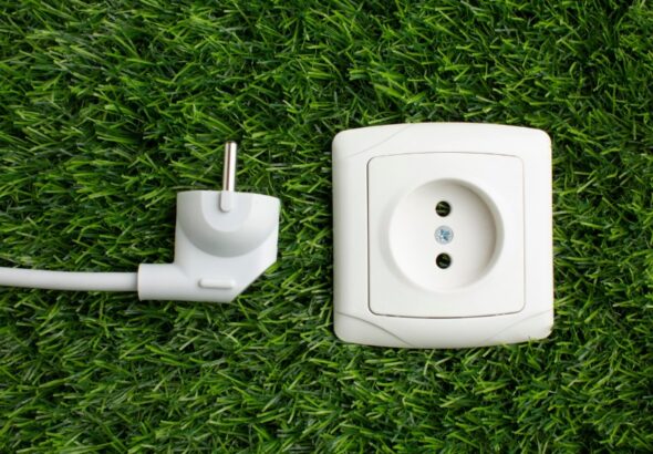 White European-style power plug and matching wall socket module placed on green artificial grass, symbolizing smart plug technology and energy-conscious home offices.