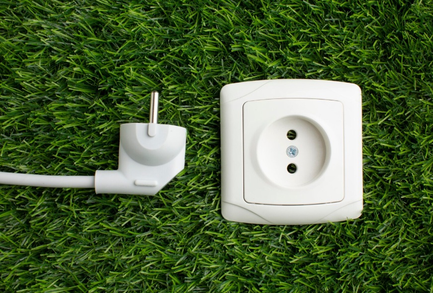 White European-style power plug and matching wall socket module placed on green artificial grass, symbolizing smart plug technology and energy-conscious home offices.