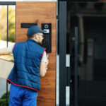 Delivery worker holding a package and using a smart lock keypad at a modern front door.
