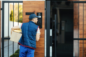 Delivery worker holding a package and using a smart lock keypad at a modern front door.