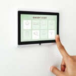 Person using a wall-mounted smart home touchscreen display to control lights, security, and connected home devices.