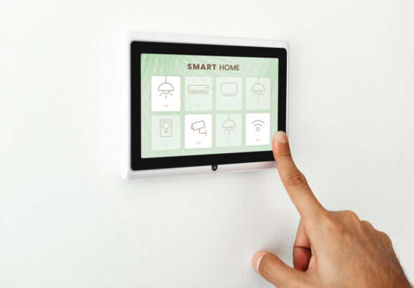 Person using a wall-mounted smart home touchscreen display to control lights, security, and connected home devices.