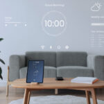 Modern smart home living room with a wall-projected digital dashboard showing weather, schedule, music controls, and clock, alongside a smart sensor tablet on a coffee table.