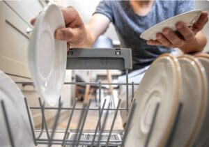 Person loading white plates into the lower rack of a dishwasher in a home kitchen.