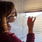 Person adjusting smart window blinds while sunlight streams through the slats, demonstrating automated light control in a modern home.