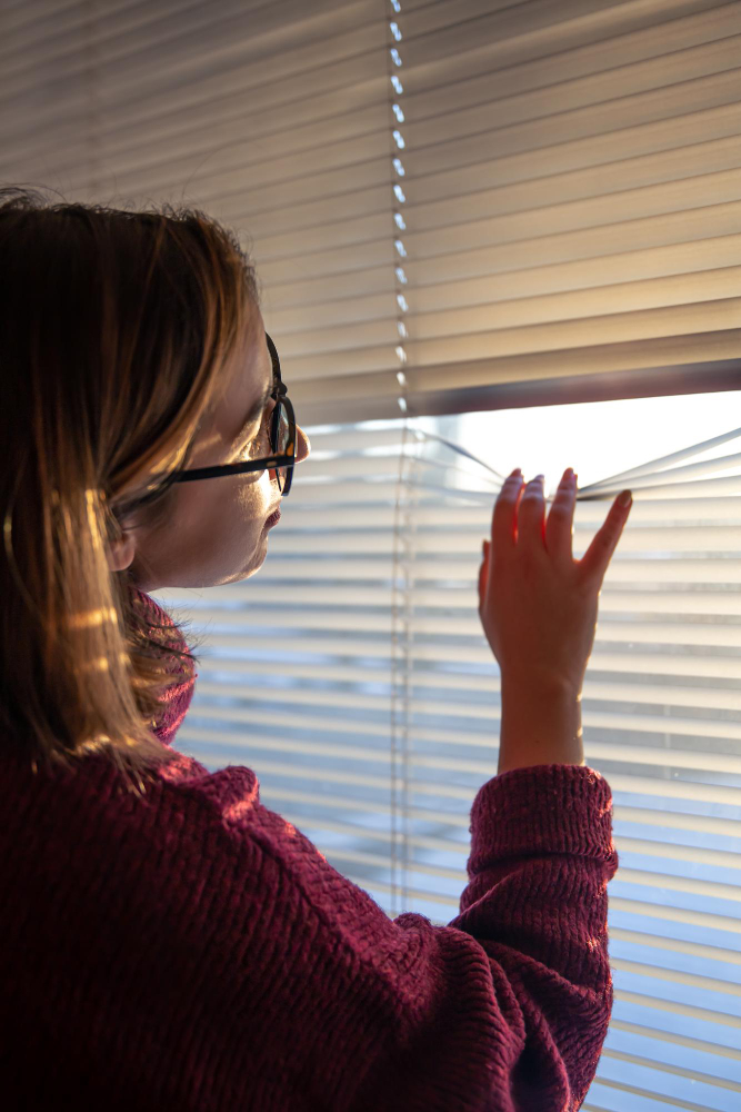 Person adjusting smart window blinds while sunlight streams through the slats, demonstrating automated light control in a modern home.
